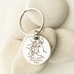 May include: Silver keychain with a round tag featuring a design of five fists bumping together. The tag is engraved with the names "Matt, Jacob, Katie, Emma, & Dad".