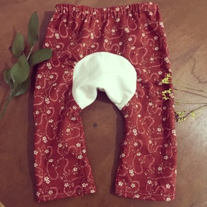 Puede incluir: Leggings de bebé de color rojo y blanco con un panel de tela blanca en la parte posterior.