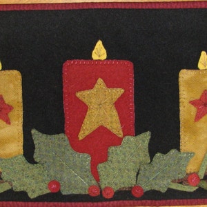 Pode incluir: Um corredor de mesa de feltro preto com três velas amarelas e estrelas vermelhas. As velas são cercadas por folhas verdes e bagas vermelhas.