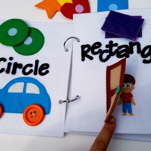 May include: A felt activity book with pages featuring shapes and objects. One page shows a blue car with orange button wheels and the word "Circle". The other page has the word "Rectangle" and a felt door with a boy.