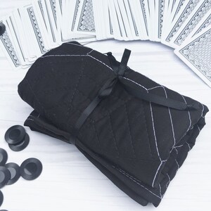 May include: A black quilted fabric pouch with a white geometric pattern and a black ribbon tied around it. The pouch is rolled up and sitting on a white surface.