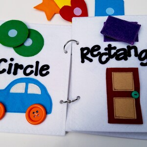 May include: Open felt book with colorful shapes and words. The left page shows a green circle with a light blue center, the word "Circle", and a blue car with orange button wheels. The right page has the word "rectangle" and a brown door.