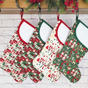 May include: Four Christmas stockings with festive patterns, including gift boxes, Santa Claus, and reindeer. Each stocking has a white cuff and is trimmed in red or green. They hang from a wooden rack with greenery.