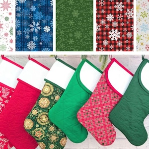 May include: A collection of Christmas stockings with various patterns, including red, green, and patterned fabrics. The stockings are hung against a white brick wall. Above the stockings are fabric swatches with snowflake designs.