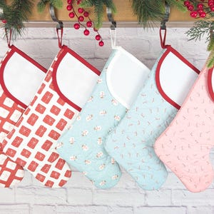 May include: Five Christmas stockings in various patterns and colors hang from a wooden rod. The stockings feature red, white, and blue designs, including gift boxes and festive patterns. Each stocking has a white cuff and red trim.