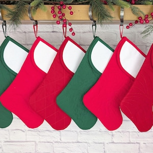 Könnte beinhalten: Sechs Weihnachtsstrümpfe in Rot und Grün mit weißen Bündchen. Die Strümpfe hängen an einer Holzstange mit Metallhaken, die mit Grün und roten Beeren verziert ist. Die Strümpfe sind gesteppt.