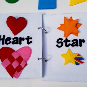 May include: A felt book with white pages and metal rings. The left page has a red heart and the word "Heart". The right page has an orange star and the word "Star". Additional felt shapes are visible.