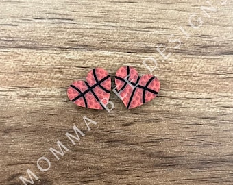 May include: Two red heart-shaped ornaments with a basketball pattern. The hearts are on a woodgrain background.