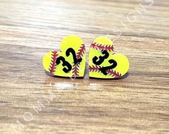 Op de afbeelding: Twee hartvormige oorbellen met een softbalontwerp. De oorbellen zijn geel met rode stiksels en het nummer 32 in zwart. Ze liggen op een houten oppervlak. De tekst "MOMMA BEE DESIGNS" staat onderaan.