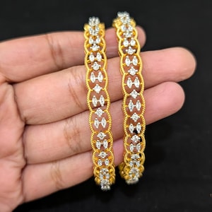 May include: Two gold bangles featuring a repeating openwork pattern of interconnected circles. Each circle is set with small, clear, marquise-cut and round-cut stones that create a sparkling, textured surface along the length of the jewelry.