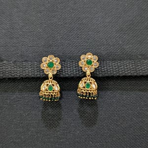 Peut inclure: Une paire de boucles d'oreilles dorées avec un motif floral. Chaque boucle d'oreille présente un dessus en forme de fleur avec des pierres transparentes entourant une pierre verte centrale. Le bas en forme de cloche est orné de pierres vertes et de détails complexes.