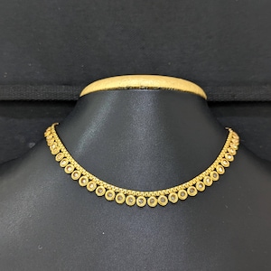 Pode incluir: Um colar dourado com uma corrente delicada e uma série de pingentes circulares espaçados. Cada pingente apresenta uma pedra transparente no centro. O colar é exibido em um manequim preto.