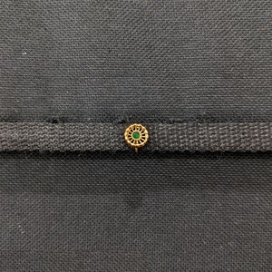 May include: A gold nose ring with a green gemstone in the centre. The ring has a delicate, intricate design.