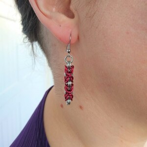 Puede incluir: Un par de pendientes de plata con un diseño de cadena roja.