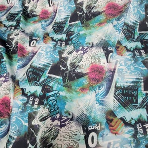 May include: A colorful fabric with a newspaper print design. The fabric features a blue, green, and pink watercolor background with black text and images. The text includes the words "feast", "break", "Pares", and "0".