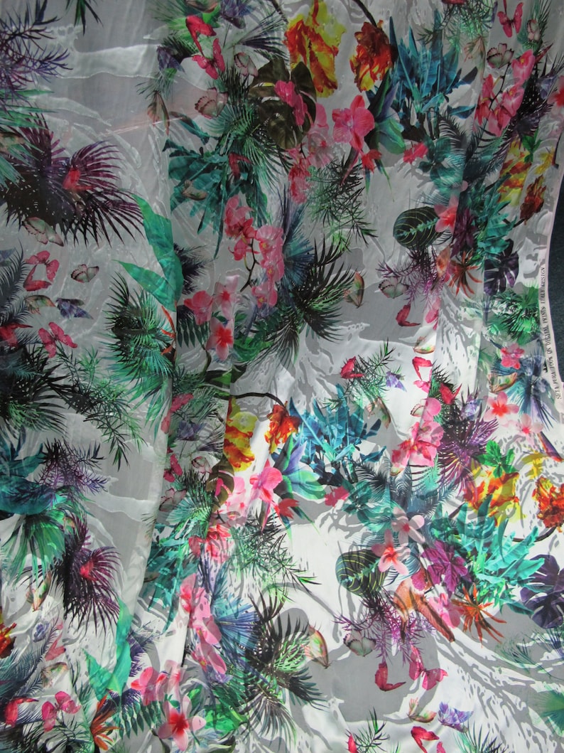 May include: White fabric with a tropical print featuring colorful flowers, leaves, and butterflies.
