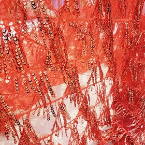 May include: Red sequined fabric with fringe trim. The fabric has a sheer, mesh-like texture and is decorated with small, round sequins.