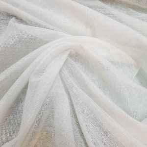 May include: White sheer fabric with a fine, woven texture. The fabric is draped and folded, showing its delicate and airy quality.