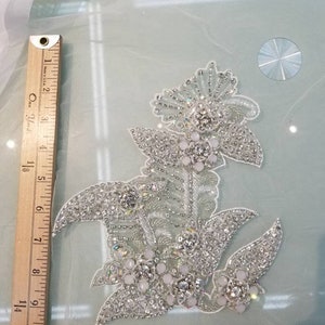 May include: A silver floral applique with white beads and rhinestones. The applique is approximately 5 inches wide and 6 inches tall.