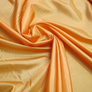 May include: A close-up of a smooth, silky fabric in a vibrant orange color. The fabric is draped and folded, showcasing its texture and sheen.
