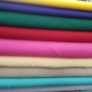 K&ouml;nnte beinhalten: Ein Stapel Stoffmuster in verschiedenen Farben, darunter Gelb, Blau, Gr&uuml;n, Rot, Pink, Beige, T&uuml;rkis und Grau.