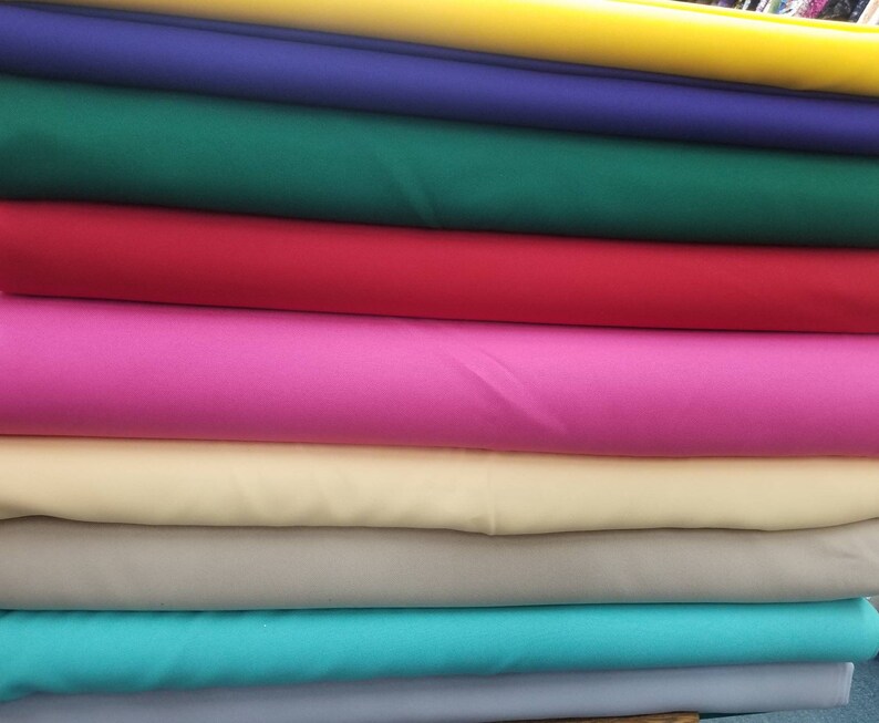 K&ouml;nnte beinhalten: Ein Stapel Stoffmuster in verschiedenen Farben, darunter Gelb, Blau, Gr&uuml;n, Rot, Pink, Beige, T&uuml;rkis und Grau.