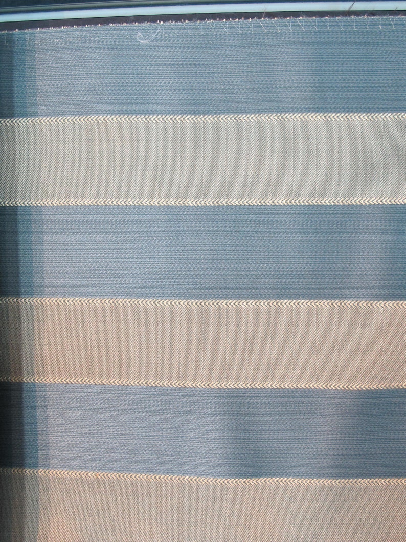 May include: A striped fabric with alternating bands of light blue and beige. The fabric has a subtle texture and a woven appearance.