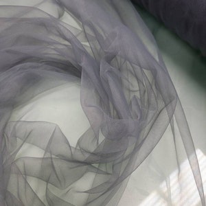 May include: A roll of soft, gray tulle fabric. The fabric is sheer and delicate, with a slightly shimmery finish.