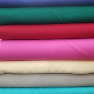 K&ouml;nnte beinhalten: Ein Stapel Stoffmuster in verschiedenen Farben, darunter Gelb, Blau, Gr&uuml;n, Rot, Pink, Beige, Grau, T&uuml;rkis und Hellblau.