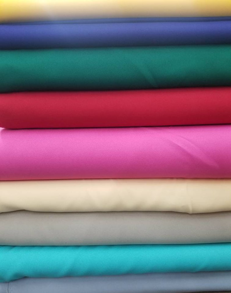 K&ouml;nnte beinhalten: Ein Stapel Stoffmuster in verschiedenen Farben, darunter Gelb, Blau, Gr&uuml;n, Rot, Pink, Beige, Grau, T&uuml;rkis und Hellblau.