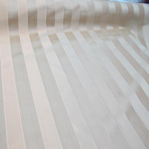 May include: A close-up of a beige and white striped fabric. The fabric has a subtle sheen and a smooth texture.