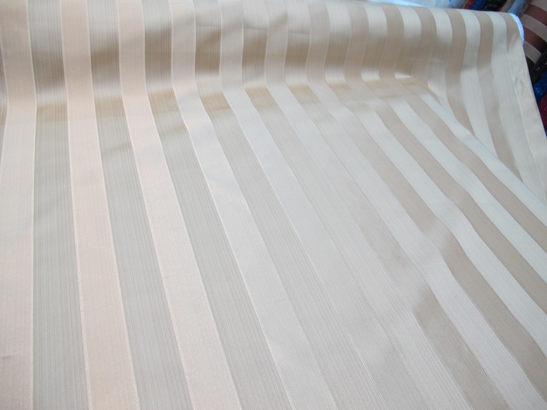 May include: A close-up of a beige and white striped fabric. The fabric has a subtle sheen and a smooth texture.