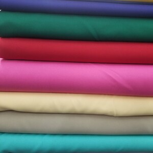 K&ouml;nnte beinhalten: Stapel von Stoffproben in verschiedenen Farben, darunter Gelb, Blau, Gr&uuml;n, Rot, Rosa, Beige, T&uuml;rkis und Grau.