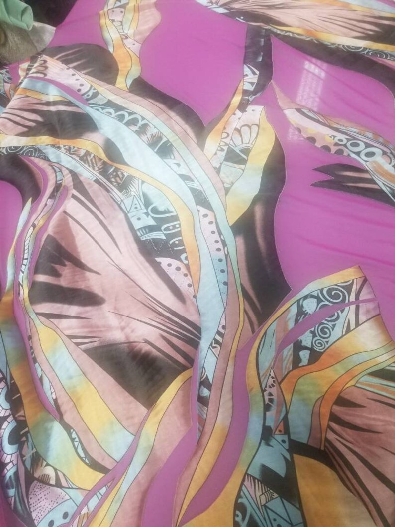 Pode incluir: Tecido abstrato com fundo rosa e um padr&atilde;o colorido e espiralado. O tecido tem um visual em camadas com diferentes tons de azul, amarelo e marrom.