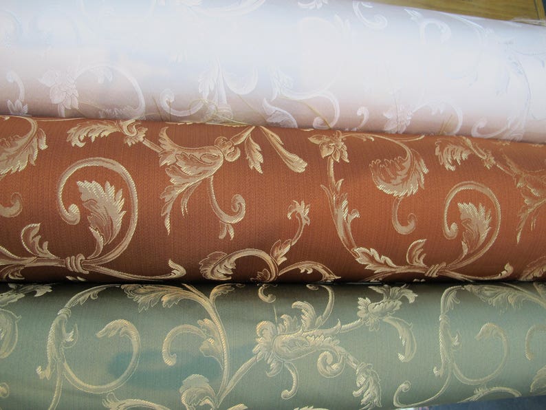 May include: Three rolls of fabric with a floral pattern. The top roll is white with a subtle pattern, the middle roll is brown with a gold pattern, and the bottom roll is green with a gold pattern.
