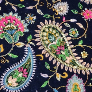 Może przedstawiać: Czarny materiał z misternymi haftami w odcieniach różowego, zielonego, niebieskiego i złotego. Wzór zawiera wzory paisley i motywy kwiatowe.