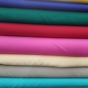 K&ouml;nnte beinhalten: Ein Stapel Stoffmuster in verschiedenen Farben, darunter Gelb, Blau, Gr&uuml;n, Rot, Pink, Beige, T&uuml;rkis und Hellblau.