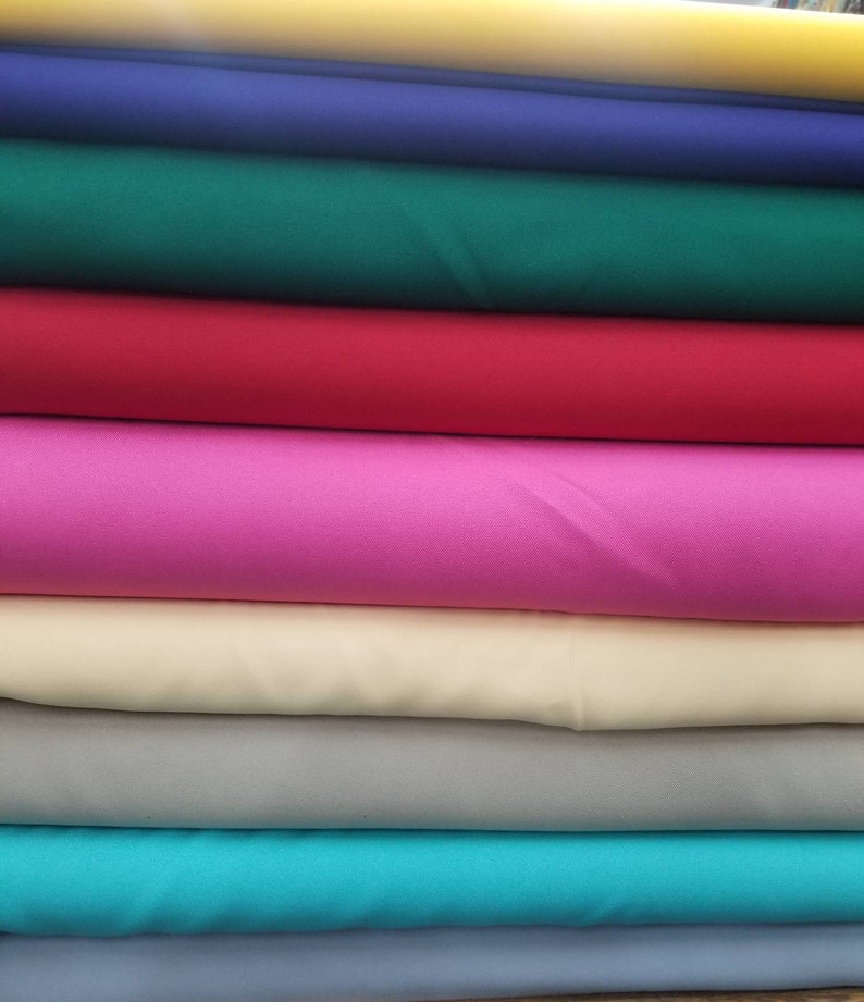 K&ouml;nnte beinhalten: Ein Stapel Stoffmuster in verschiedenen Farben, darunter Gelb, Blau, Gr&uuml;n, Rot, Pink, Beige, T&uuml;rkis und Hellblau.