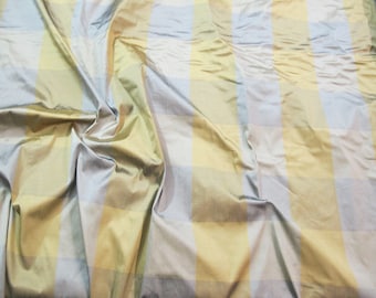 May include: A close-up of a fabric with a checkered pattern in shades of yellow, light blue, and white. The fabric is wrinkled and has a silky sheen.