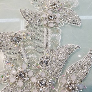 May include: A delicate floral design with white beads and clear rhinestones. The design is on a sheer, light green fabric.