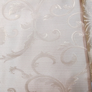 May include: A close-up of a beige fabric with a subtle, embossed pattern of swirling leaves and vines. The fabric has a slightly textured surface.