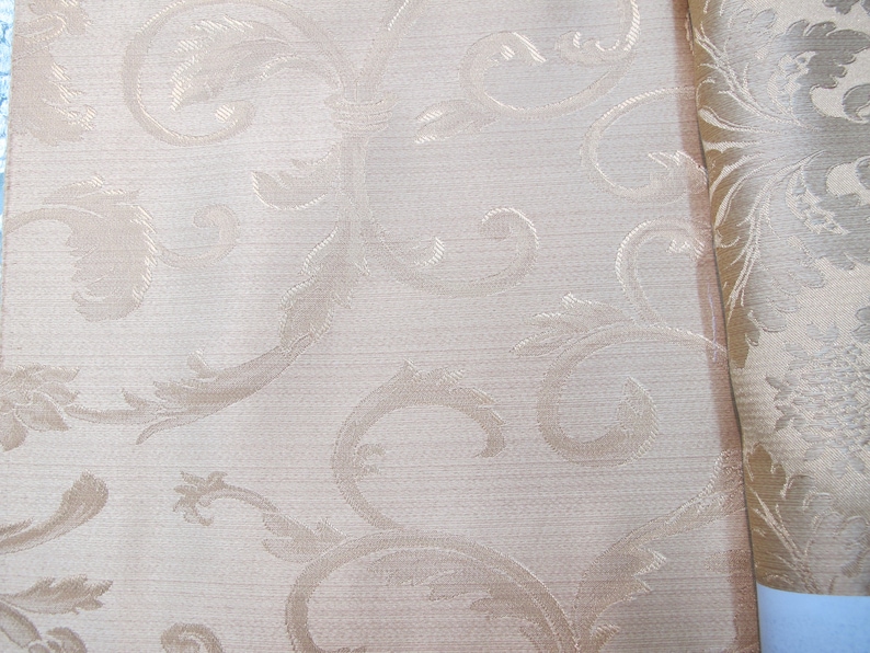 May include: A close-up of a beige fabric with a subtle, embossed pattern of swirling leaves and vines. The fabric has a slightly textured surface.