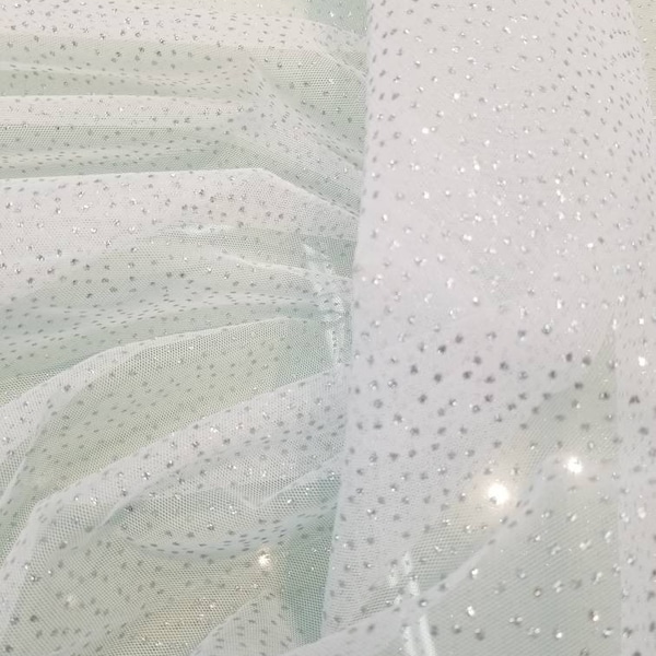 Glitter sparkle tulle usable for apparel accessories interior designs  dancing costumes. 60" wide White base with silver glitter polka dots.