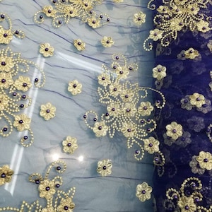 Puede incluir: Tela de malla morada con bordado dorado y cuentas moradas. La tela tiene un diseño floral.