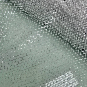 May include: Silver metallic mesh fabric with a diamond pattern. The fabric is folded in half, creating a diagonal line across the image.