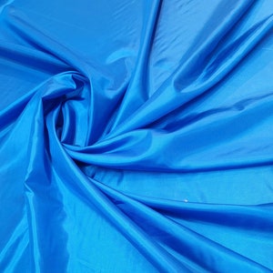 Pode incluir: Um close-up de um tecido azul brilhante com uma textura lisa e sedosa. O tecido está dobrado e drapeado, criando linhas suaves e fluidas.