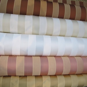 Op de afbeelding: Vier rollen gestreepte stof in verschillende kleuren, waaronder bruin, beige, wit en roze.