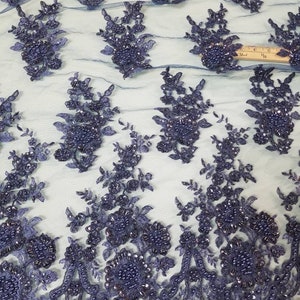 May include: Navy blue beaded lace fabric with a floral design. The lace is delicate and intricate, with small beads scattered throughout. The fabric is perfect for adding a touch of elegance to any project.