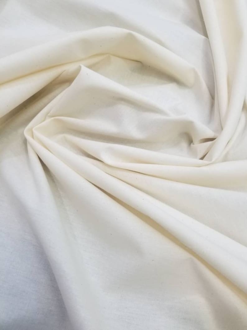 Puede incluir: Primer plano de una tela de algod&oacute;n blanca con una textura suave. La tela est&aacute; doblada y drapeada, mostrando su aspecto suave y natural.