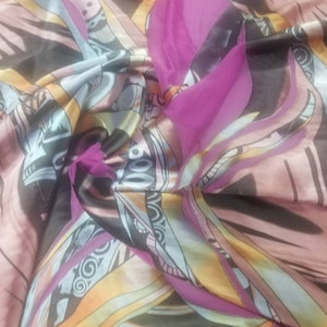 Pode incluir: Um tecido estampado colorido com um design rosa, azul, amarelo e preto. O tecido &eacute; feito de um material macio e sedoso e tem uma textura fluida e drapeada.